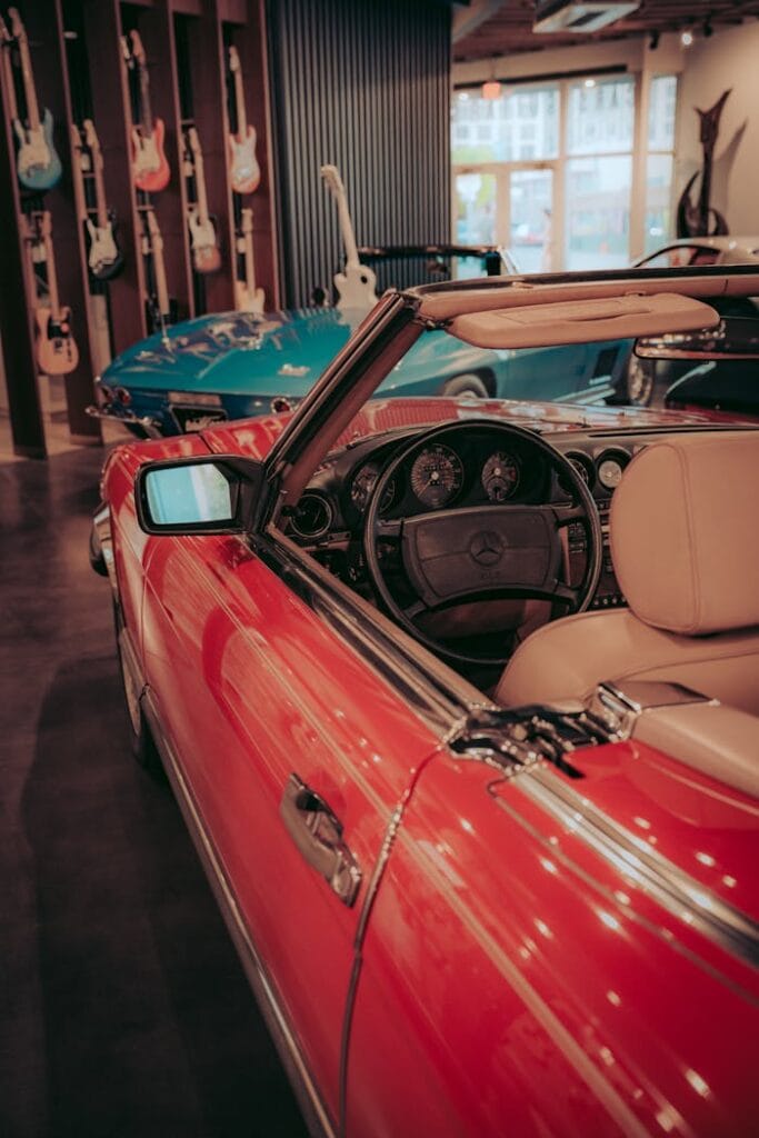 A red classic Mercedes convertible parked indoors with guitars in the background.